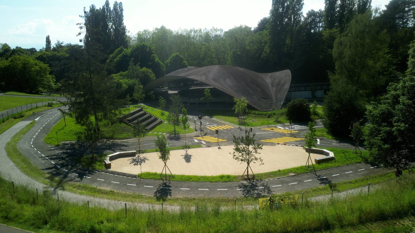 Vue d’ensemble du jardin : pistes, stabilisé planté de jeunes pins, gradins et coupole