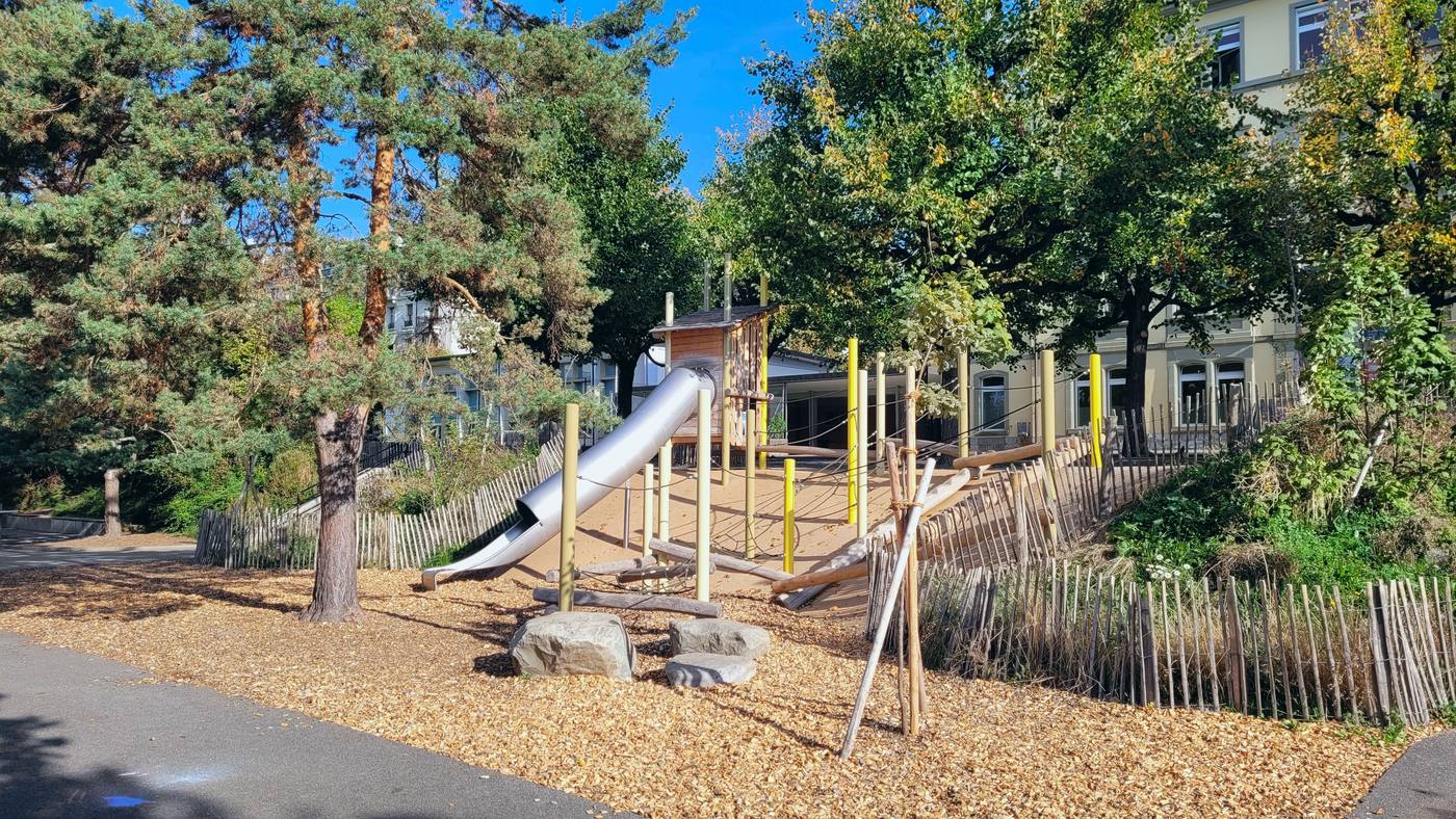 Butte de jeux avec toboggan, cabane et parcours d’équilibre sous les grands arbres