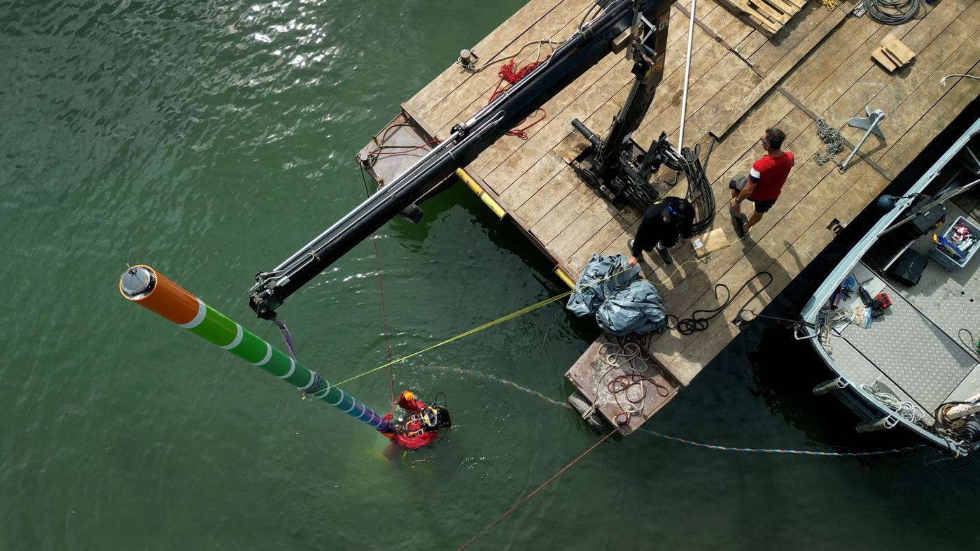 Vue aérienne d’un plongeur posant un mât coloré depuis une barge